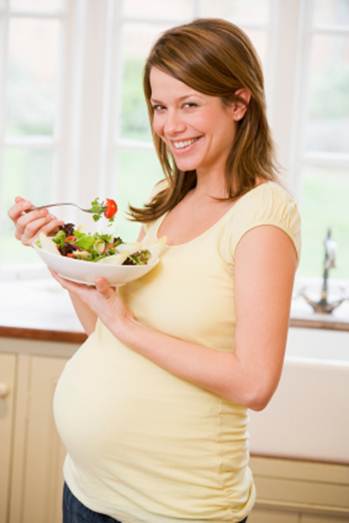 Description: Pregnant woman in kitchen eating a salad 
